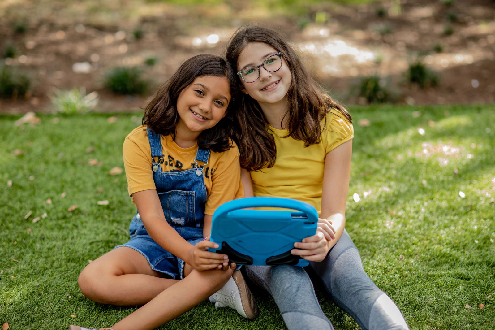 Two girls sit in the grass playing on a blue tablet. What does their gaming say about them? Discover more about the type of gamer your child is inside.