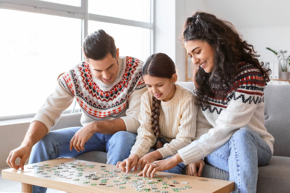 A mom, dad, and child working on a puzzle on a table.
